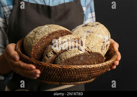 Donna in possesso di pane appena sfornato su sfondo nero, primo piano Foto Stock