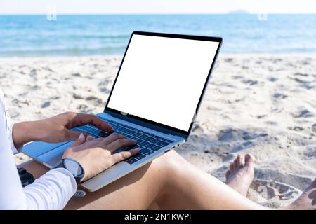 Concetto di lavoro da qualsiasi luogo. Vista posteriore della giovane donna che lavora su un computer portatile sulla spiaggia Foto Stock