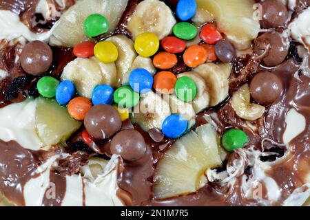 Miscela di cioccolato con biscotti e diversi tipi di pezzi di cioccolato e crema con ananas fresco e pezzi di banane sulla parte superiore su una torta di pasta Foto Stock