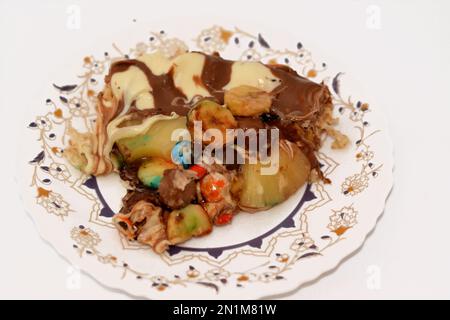 Miscela di cioccolato con biscotti e diversi tipi di pezzi di cioccolato e crema con ananas fresco e pezzi di banane sulla parte superiore su una torta di pasta Foto Stock