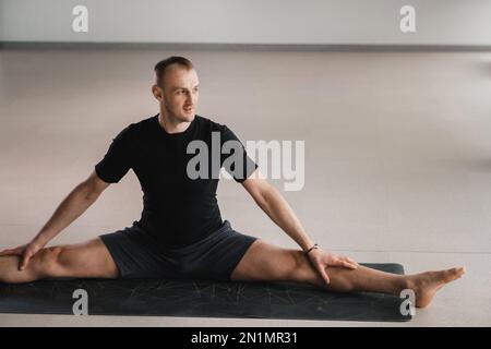 Un uomo di costruzione atletica fa yoga in palestra su un tappetino. Foto Stock
