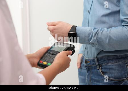 Uomo che usa l'orologio intelligente per il pagamento senza contatto tramite il terminale al chiuso, primo piano Foto Stock