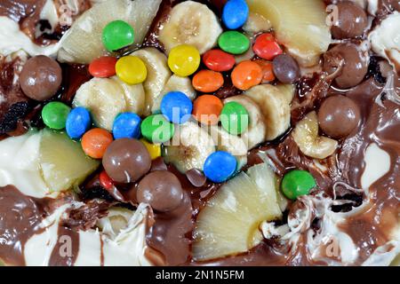 Miscela di cioccolato con biscotti e diversi tipi di pezzi di cioccolato e crema con ananas fresco e pezzi di banane sulla parte superiore su una torta di pasta Foto Stock