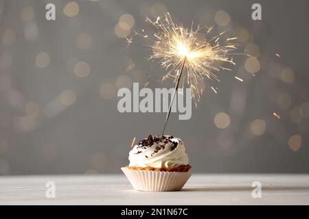 Delizioso dessert con scintillanti scintillanti su un tavolo di legno bianco contro le luci sfocate Foto Stock