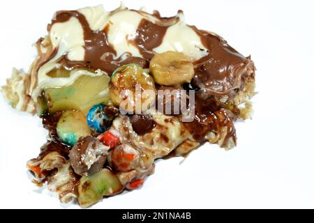 Miscela di cioccolato con biscotti e diversi tipi di pezzi di cioccolato e crema con ananas fresco e pezzi di banane sulla parte superiore su una torta di pasta Foto Stock