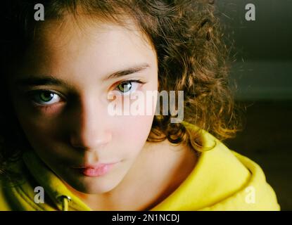 Una giovane ragazza dagli occhi verdi sta guardando in su mentre il suo volto rimane nella mezza ombra Foto Stock