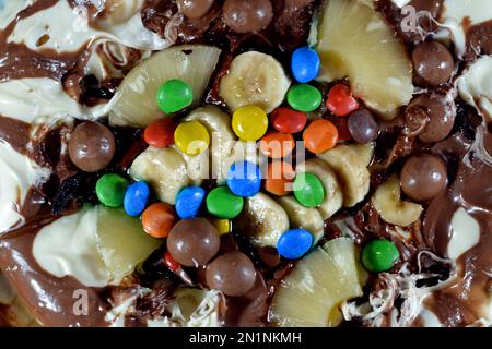 Miscela di cioccolato con biscotti e diversi tipi di pezzi di cioccolato e crema con ananas fresco e pezzi di banane sulla parte superiore su una torta di pasta Foto Stock