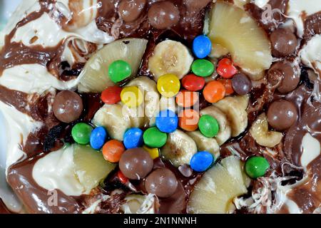 Miscela di cioccolato con biscotti e diversi tipi di pezzi di cioccolato e crema con ananas fresco e pezzi di banane sulla parte superiore su una torta di pasta Foto Stock