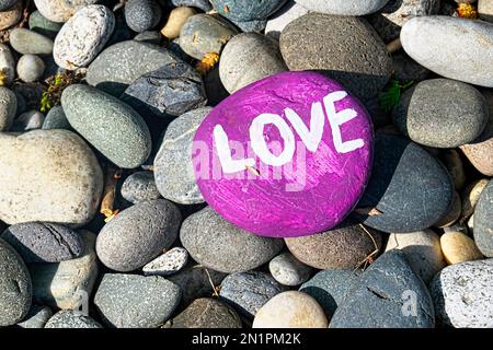 Una roccia, o pietra dipinta di viola con la parola 'AMORE' dipinta di bianco accoccolato sulla sommità di uno strato di rocce simili. Foto Stock