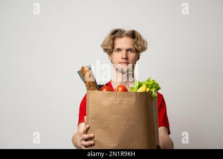 Servizio di consegna cibo concetto. Handsome consegna uomo, corriere che trasporta il sacchetto del pacchetto del cibo e delle bevande della drogheria dal deposito, supermercato isolato sopra Foto Stock
