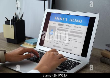 Donna che utilizza il computer portatile per compilare il modulo di domanda di patente di guida al tavolo in ufficio, in primo piano Foto Stock