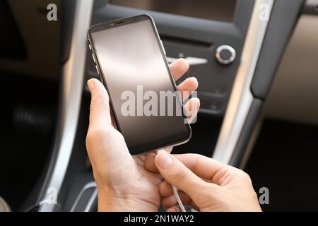 Donna che collega il cavo di ricarica allo smartphone in auto, in primo piano Foto Stock