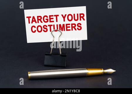 Concetto aziendale. Sulla superficie nera è una penna, una clip di carta dell'ufficio con un biglietto da visita su cui è scritto - Target i vostri clienti Foto Stock