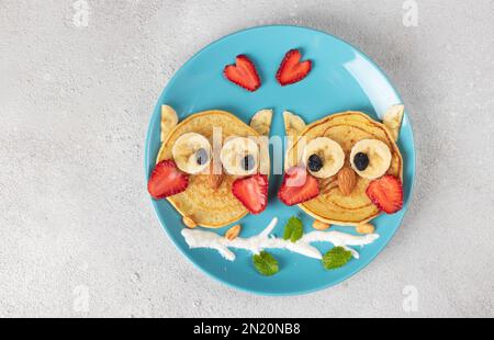 Frittelle a forma di gufo con fragole, banane e mandorle, una colazione creativa per bambini o San Valentino, vista dall'alto Foto Stock