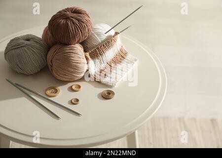 Palle di filato, bottoni e aghi per maglieria su tavolo bianco all'interno. Hobby creativo Foto Stock