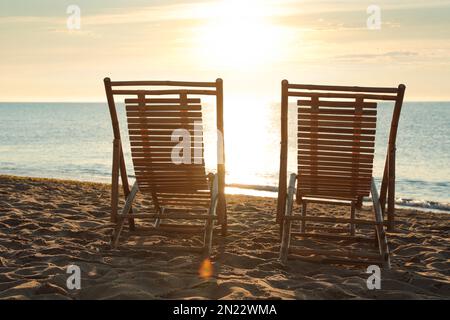 Sedie a sdraio in legno sulla spiaggia sabbiosa al tramonto. Vacanze estive Foto Stock