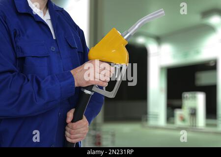 Lavoratore che tiene ugello di combustibile vicino stazione di benzina, primo piano Foto Stock