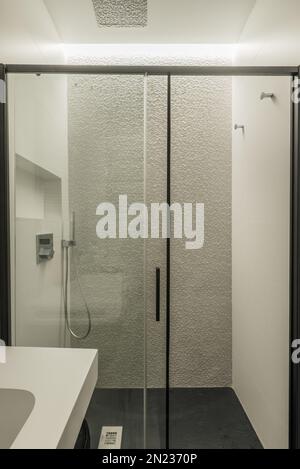 Cabina doccia con piastrelle bianche ruvide, divisorio scorrevole in vetro con profili in metallo nero e piatto doccia in ardesia nera Foto Stock