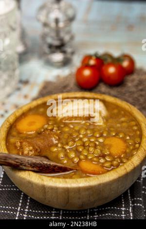 Un delizioso stufato tradizionale spagnolo di lenticchie con chorizo e verdure in una ciotola di legno di bambù su un panno nero Foto Stock