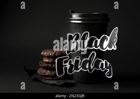Tazza da caffè in carta da asporto con frase Black Friday e biscotti su sfondo scuro Foto Stock