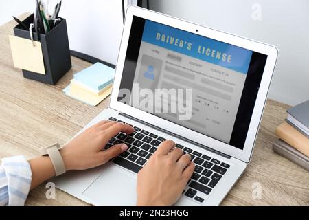 Donna che utilizza il computer portatile per compilare il modulo di domanda di patente di guida al tavolo in ufficio, in primo piano Foto Stock