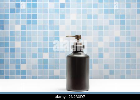 Ciotola in porcellana nera con dispenser di sapone per il lavaggio delle mani in un bagno piastrellato blu Foto Stock