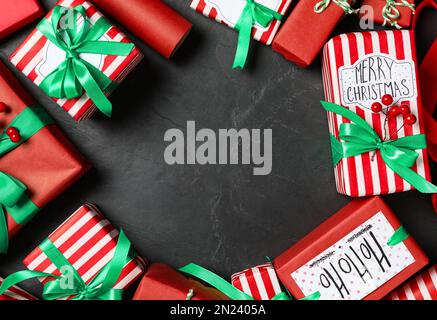 Cornice delle scatole regalo di Natale con archi verdi su sfondo grigio scuro, piatto. Spazio per il testo Foto Stock