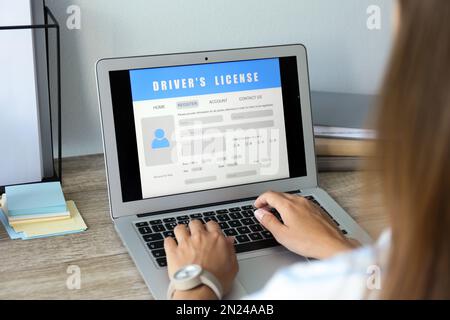 Donna che utilizza il computer portatile per compilare il modulo di domanda di patente di guida al tavolo in ufficio, in primo piano Foto Stock
