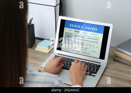 Donna che utilizza il computer portatile per compilare il modulo di domanda di patente di guida al tavolo in ufficio, in primo piano Foto Stock