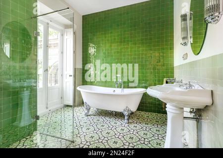 Bel bagno decorato in stile vintage con vasca da bagno a artiglio, piastrelle idrauliche sul pavimento e pareti verdi Foto Stock