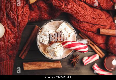 Composizione piatta con bicchiere di cacao saporito e canna da zucchero natalizia su tavola di legno Foto Stock