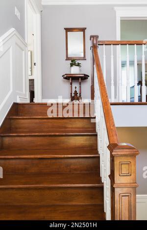 Scale in legno di ciliegio e corrimano con mandrini bianchi che conducono al piano superiore all'interno di una casa in stile cottage contemporaneo. Foto Stock