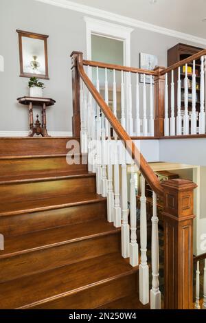 Scale in legno di ciliegio e corrimano con mandrini bianchi che conducono al piano superiore all'interno di una casa in stile cottage contemporaneo. Foto Stock