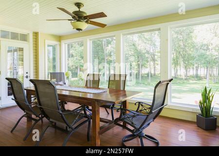 Tavolo da pranzo in legno antico e sedie con schienale alto nella sala da sole con pavimento in legno di cedro colorato all'interno di una casa in stile cottage contemporaneo. Foto Stock