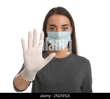 Donna con maschera protettiva e guanti medici che mostrano un gesto di arresto su sfondo bianco, concentrarsi sulla mano Foto Stock