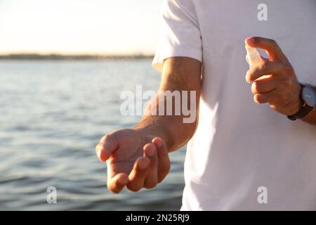 Uomo che usa repellente per insetti vicino al mare nelle giornate di sole, primo piano Foto Stock