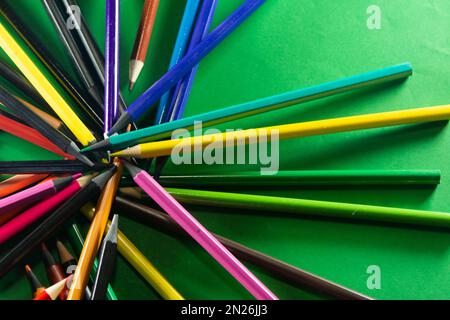 Diversi pastelli sparsi intorno. Isolato su sfondo verde. Primo piano. Foto Stock