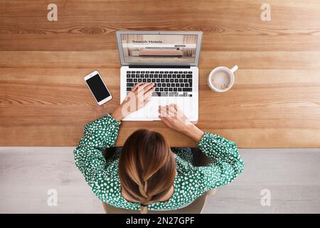 Donna che cerca un hotel usando un computer portatile al tavolo, vista dall'alto. Servizio di prenotazione online Foto Stock