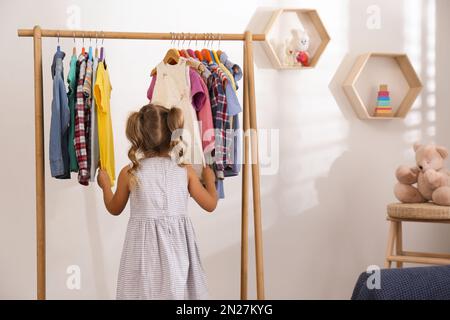 Bambina che sceglie i vestiti sulla rastrelliera in camera Foto Stock