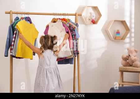 Bambina che sceglie i vestiti sulla rastrelliera in camera Foto Stock