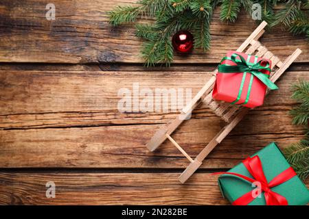 Composizione piatta con slitta, rami di abete e scatole regalo su tavolo di legno, spazio per testo Foto Stock