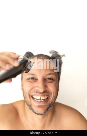 Bell'uomo dai capelli grigi taglia i capelli con un regolacapelli elettrico. Foto Stock