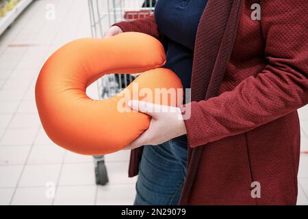 Donna incinta in maschera contro il virus compra cuscino in negozio per sostenere il collo Foto Stock