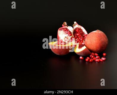 Frutto melograno spezzato con una dispersione di semi e pezzi di pesca matura su fondo nero. Primo piano. Foto Stock