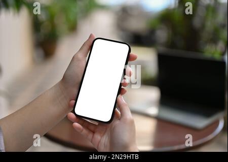 Immagine della mano in primo piano, Le mani di una donna che tiene lo schermo bianco di uno smartphone beffano su sfondo sfocato. Foto Stock