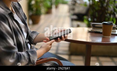 Immagine ravvicinata di una donna asiatica freelance che lavora in remoto al bar, seduto fuori del bar e utilizzando il suo smartphone. vista laterale Foto Stock