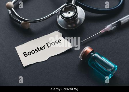 Messa a fuoco selettiva dello stetoscopio. Siringa, un flacone di vaccino e un foglio di carta scritto con Booster dose. Foto Stock