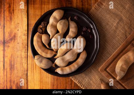 Tamarind frutta (Tamarindus indica) su tavola rustica di legno. Frutta tropicale molto apprezzata in molti paesi del mondo. Immagine di primo piano. Foto Stock