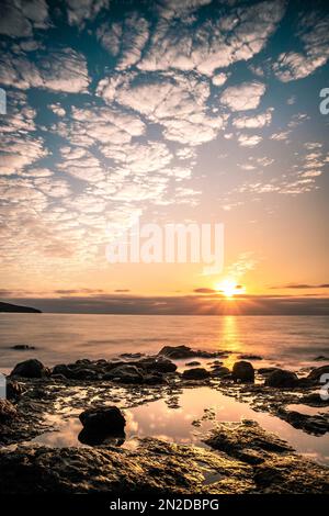 Alba, sul mare in una baia rocciosa, nuvole, lunga esposizione, controluce, roccia vulcanica, Fuerteventura, Isole Canarie, Spagna Foto Stock