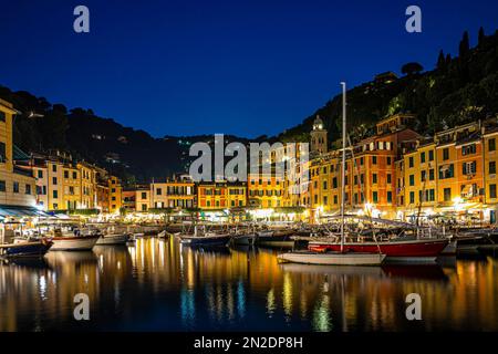 Le barche ancorano al porto di Portofino di notte di fronte alle facciate illuminate di case color pastello, Portofino, Liguria, Italia Foto Stock